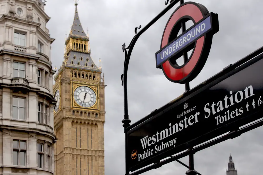 close up of the london underground sign at westminster station entrance with big ben clock tower in the background