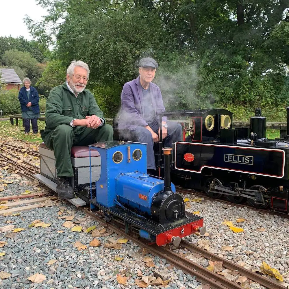 two men sitting on miniature trains on a mini railway