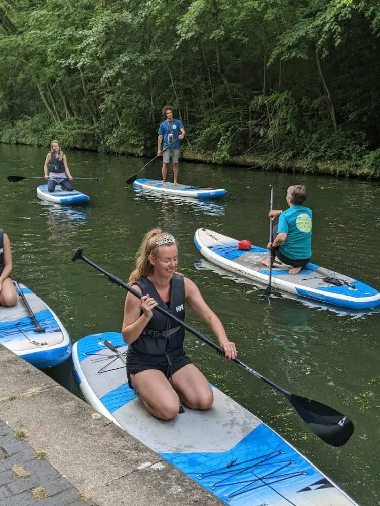 closeup of five people paddleboarding on a narrow section of river surrounded by woodland in aldridge, england