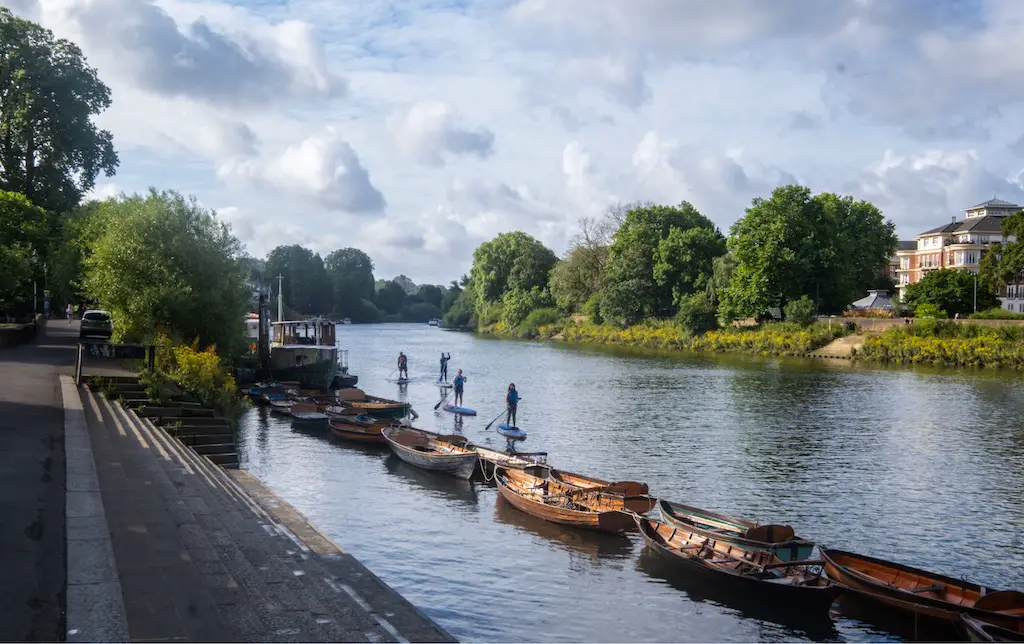 view of the river severn with small boats moored on one side and four people paddleboarding in the distance