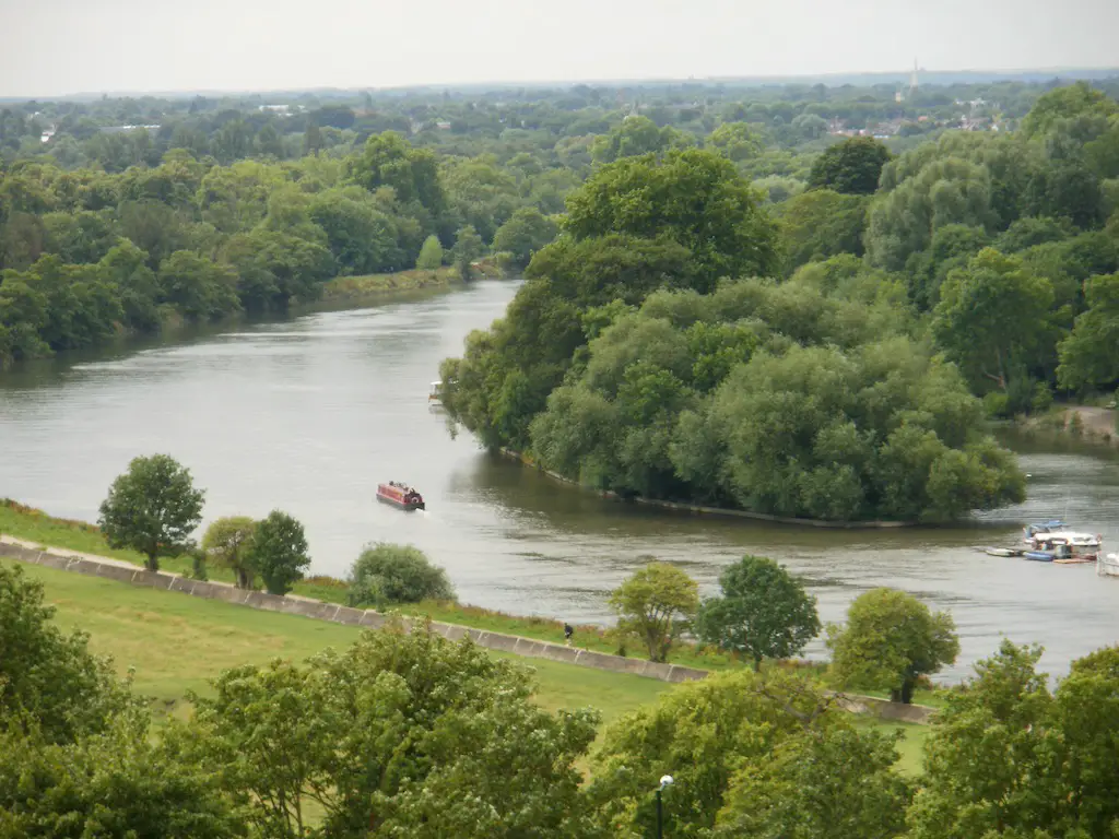 wide view of the river bend in london with a barge on the river and lots of greenery surroundings