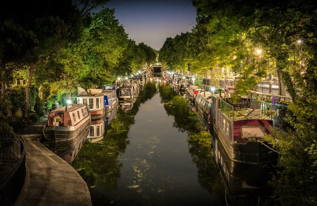 night time shot of a canal with lit up barges lining both sides at little venice, london