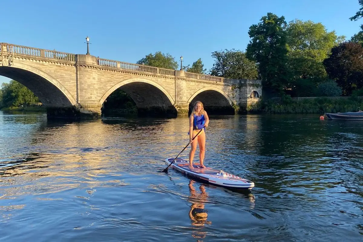 a woman paddleboarding on the river in front of kew bridge in london