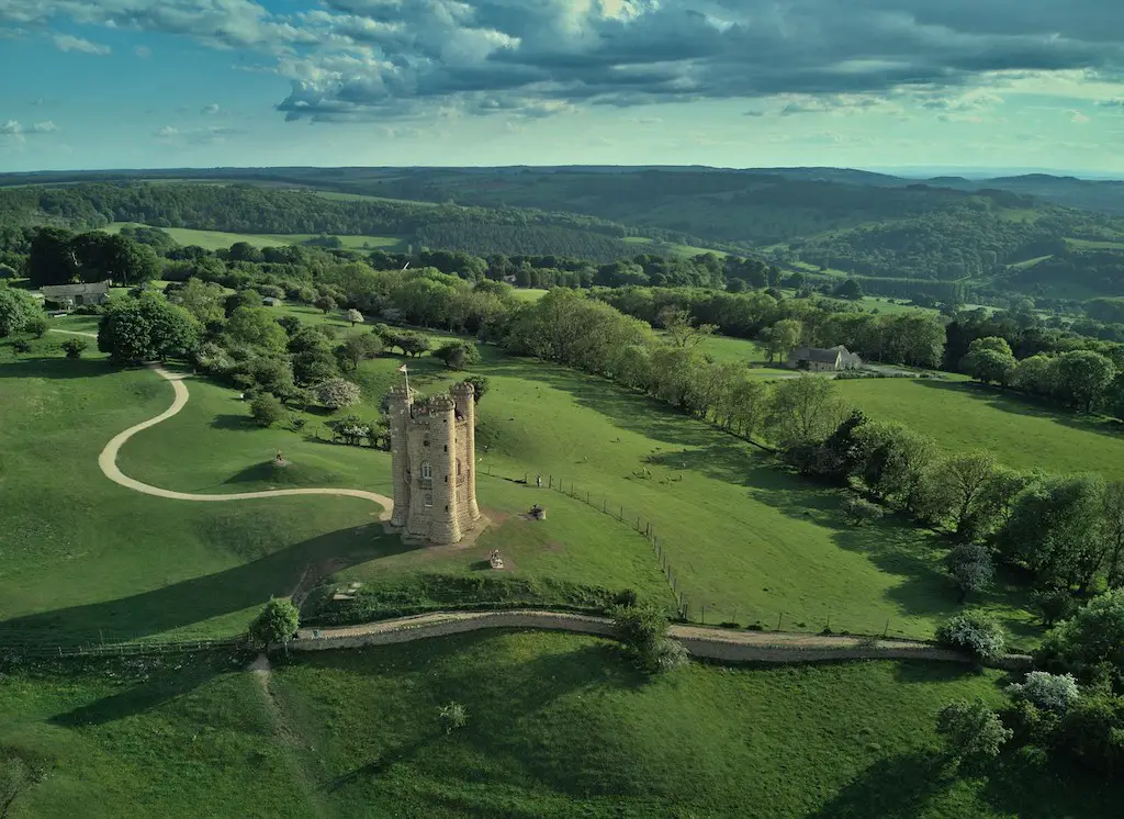 aerial views of a tall narrow castle in the middle of vast countryside at the cotswolds in england