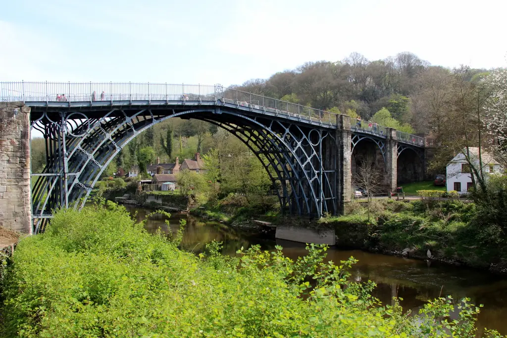 view from the left side of the river Severn banks of the iconic Victorian iron bridge over the Severn Gorge, with a few houses, hills and trees in the background