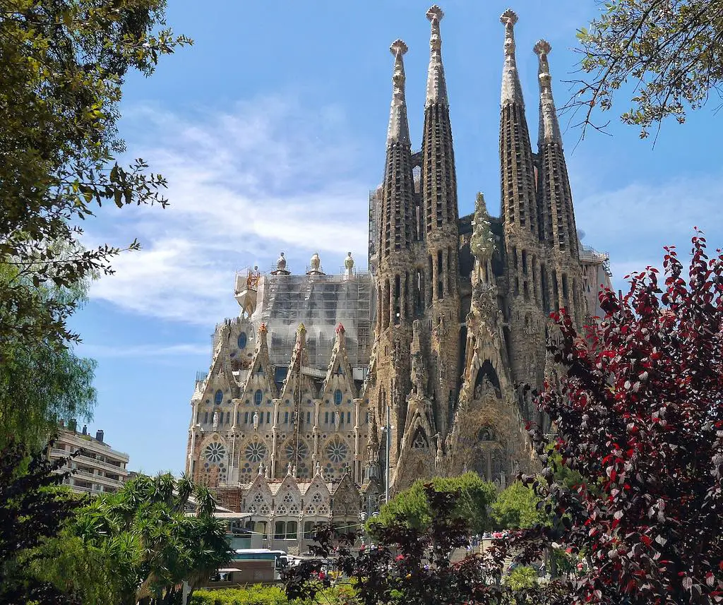 the sagrada familia in barcelona,in the background with trees and bushes paritlaly concealing in at the forefront