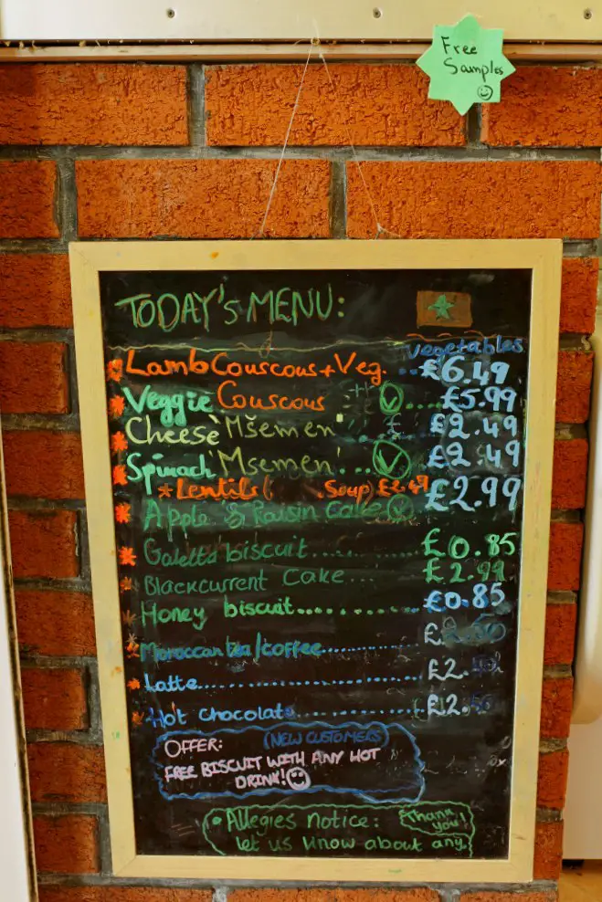 wooden framed chalkboard on a brick wall displaying the menu for Moroccan Foods, written in different coloured chalks